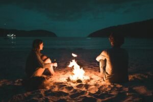 man and woman with bone fire sitting on seashore